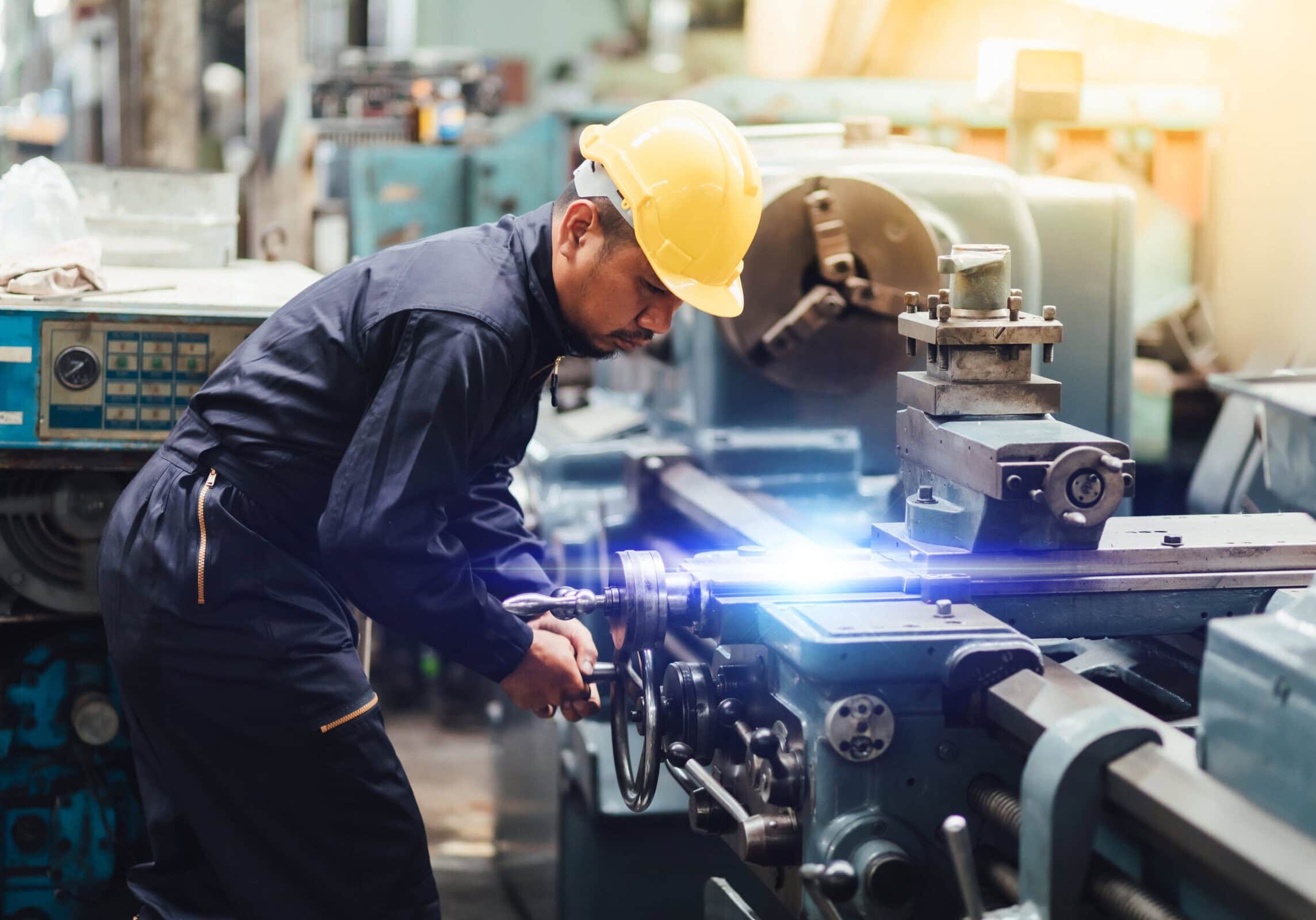 Factory Asian male worker. Asian man Lathe worker in production plant drilling at machine on the factory. Yellow hard hat safety first at mechanic factory.