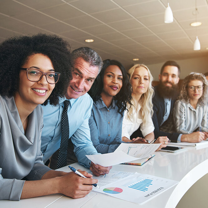 Portrait of a smiling group of diverse corporate colleagues standing in a row together at a table in a bright modern office