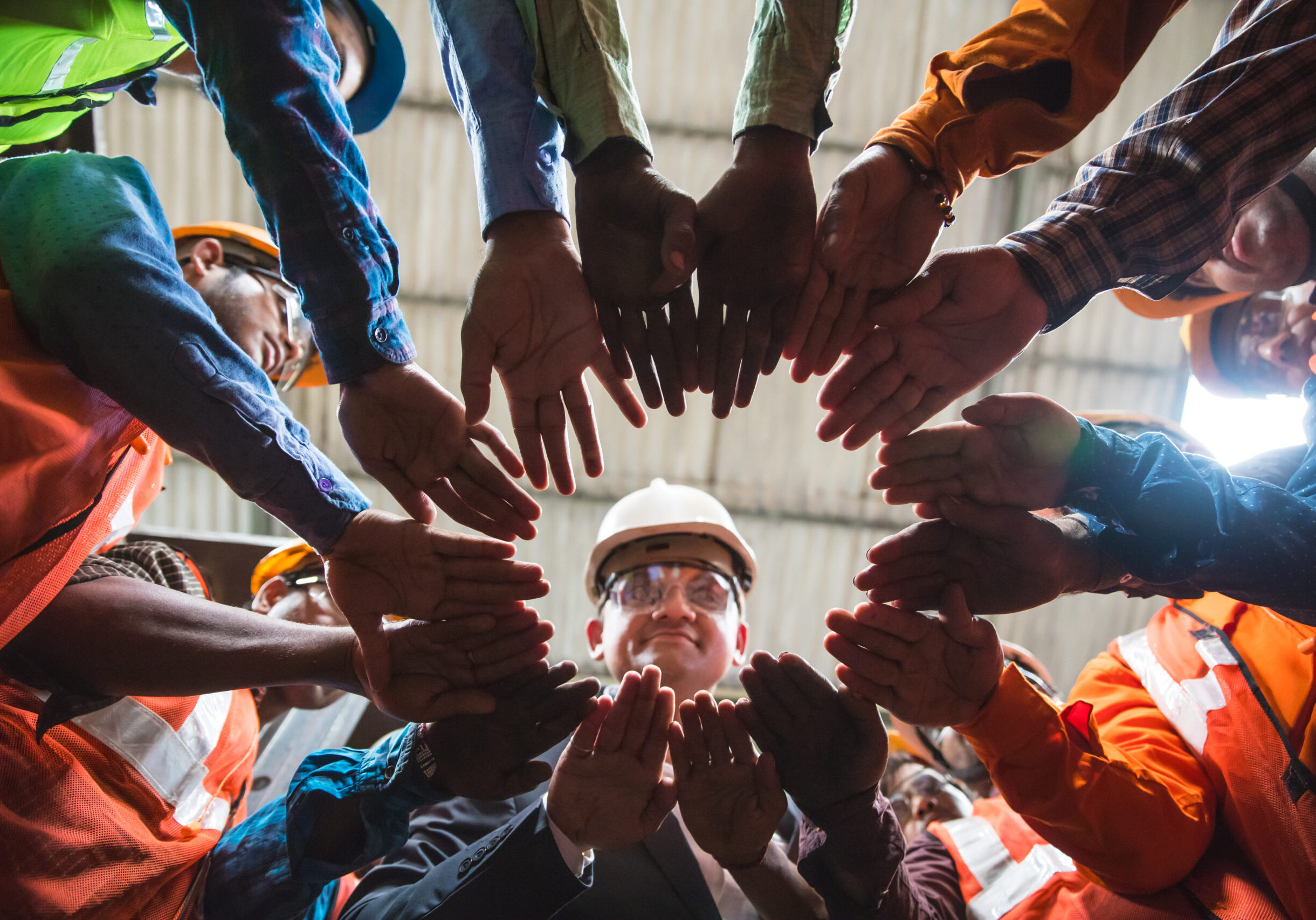 Owner looking down towards the camera in the center, with all his factory employees huddled up in a circle with their arms in the center.