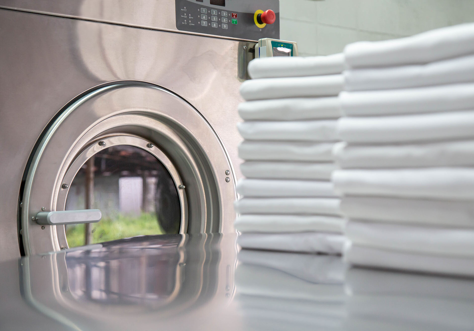 Stack of clean bed sheets in front of industrial washing machine. Focused on washing machines.